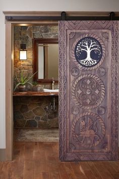 an open door leading to a bathroom with stone walls and wood flooring that has a tree on it