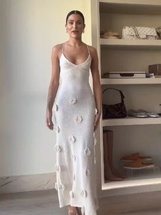 a woman in a white dress standing next to a book shelf with shoes on it