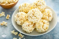 popcorn balls on a white plate next to a bowl of popcorn