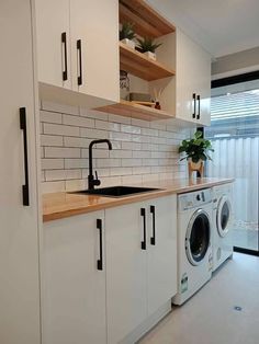 a washer and dryer in a kitchen with white cupboards next to a window