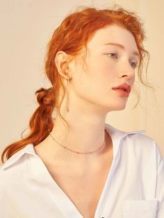 a woman with red hair is wearing a white shirt and has a necklace on her neck