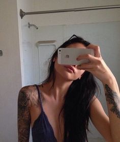 a woman taking a selfie with her phone in front of her face and tattoos on her arms