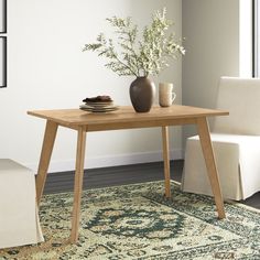 a wooden table sitting on top of a rug next to a white chair and potted plant