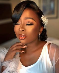 a woman in a white dress with her hand on her chin and wearing a flower hair clip