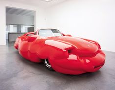 an orange car is parked in a large room with white walls and flooring on the sides