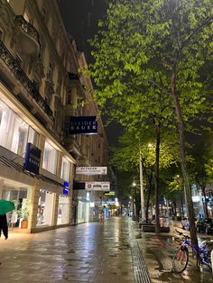 a city street at night with people walking on the sidewalk and bicycles parked in front of buildings