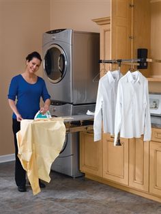 a woman ironing clothes in a kitchen with a dryer and washing machine behind her