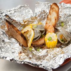 there is a sandwich with clams and corn on the cob in aluminum foil