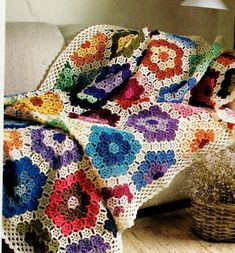 a crocheted granny's afghan sits on a couch next to a basket and lamp