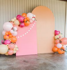 an arch made out of balloons and flowers on the floor in front of a wall