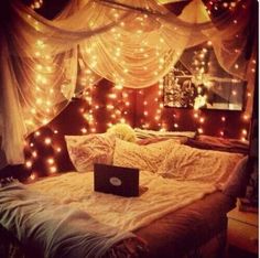 a laptop computer sitting on top of a bed covered in fairy lights and drapes