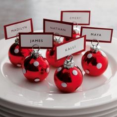 red and white ornaments with name tags on them sitting on a plate in front of stacks of plates