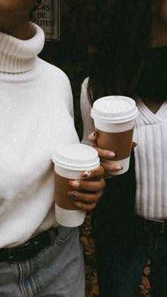 two women standing next to each other holding coffee cups