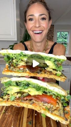 a woman holding up two sandwiches on top of a wooden cutting board