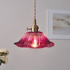 a pink light hanging from a ceiling in a room with white flowers and pictures on the wall