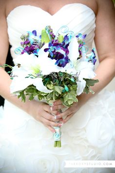 a bride holding a bouquet of white and purple flowers in her hands with green leaves