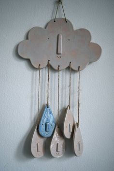 a cloud shaped clock hanging from the side of a wall with raindrops attached to it