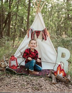 a little boy sitting in front of a teepee