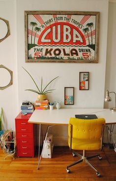 a desk with a yellow chair in front of it and a poster on the wall