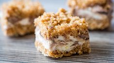 three pieces of dessert sitting on top of a wooden table with white frosting and crumbs