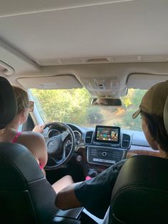 two people sitting in the driver's seat of a car looking at an electronic device