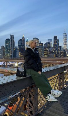 a woman sitting on the edge of a bridge in front of a cityscape