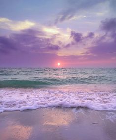 the sun is setting over the ocean with waves coming in to shore and purple clouds