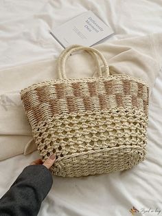 a person reaching for a straw bag on top of a white bed with an envelope