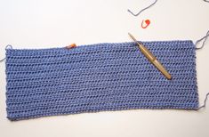 a crocheted blue piece of cloth next to a pair of scissors and thread