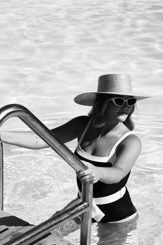 a woman in a bathing suit and hat sitting on the edge of a pool