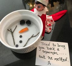 an elf is sitting next to a bowl of water with a snowman in it