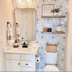 a white toilet sitting under a bathroom mirror next to a wall mounted shelf filled with towels