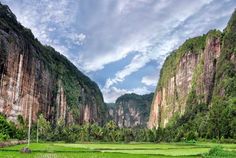 a lush green field with mountains in the background on a cloudy day, surrounded by trees and greenery