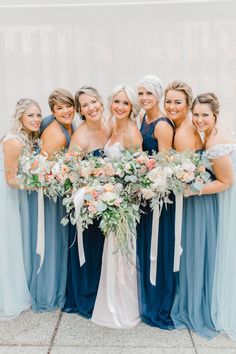 a group of women standing next to each other wearing dresses and holding bouquets in their hands