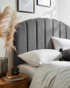 a bed with white pillows and gray headboard next to two pictures on the wall