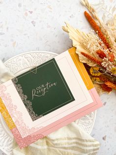 an empty card sits on a plate next to some dried flowers and a napkin with the word congratulations