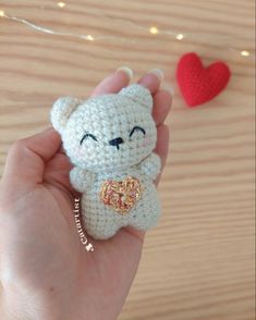 a hand holding a small crocheted teddy bear with a heart in the background