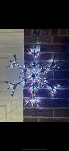 a lighted snowflake hanging from the side of a brick wall in front of a door