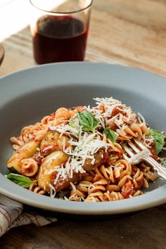 a plate of pasta with tomato sauce and parmesan cheese on top, next to a glass of red wine