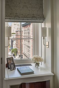 a desk with a laptop and flowers on it in front of a window