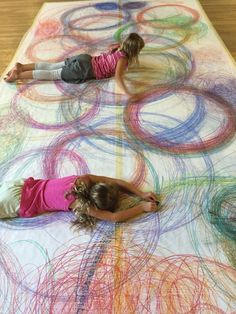 two children laying on a large sheet of colored paper with circles in the middle and one child standing next to it