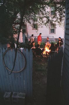 a group of people sitting around a fire pit in a yard next to a house