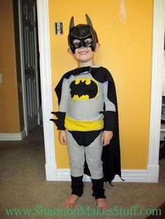 a young boy dressed as batman standing in front of a yellow wall with his hands on his hips