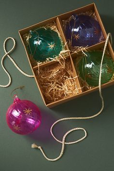 three ornaments in a box on a green surface next to a string and twine