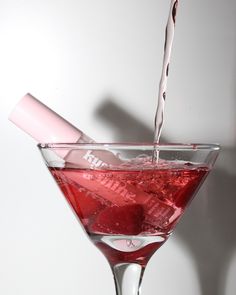 a martini glass filled with red liquid being poured into it