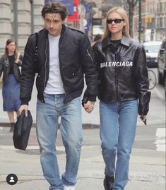 a man and woman are walking down the street holding hands while wearing black leather jackets