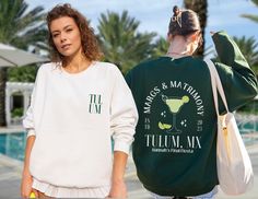 two women standing next to each other in front of a pool wearing matching sweatshirts