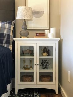 a white cabinet with glass doors in a bedroom next to a bed and lamp on the nightstand