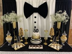 a black and white dessert table topped with cake, candies and candy balls in gold vases