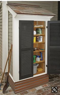 an outdoor storage shed with black shutters on the doors and shelves in front of it